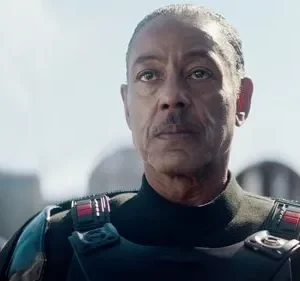 Homem de meia-idade, com bigode e olhar sério, veste uniforme escuro com armadura. Fundo de céu claro e edificações futuristas.