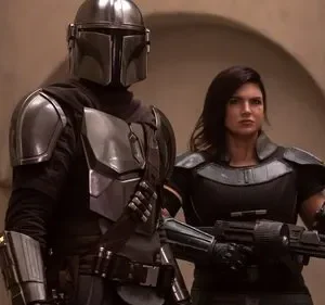 Um guerreiro blindado e uma mulher forte com arma futurista, em cenário desértico. Clima de ação e aventura.