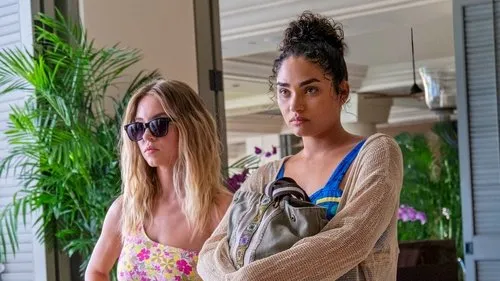 The White Lotus – T01E03: Macacos Misteriosos 1 Duas mulheres em um resort. Uma loira de óculos e top floral;a outra com coque e expressão tensa,segurando uma bolsa.