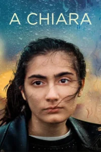 Close-up de uma jovem com expressão séria e cabelos escuros. Gotas de chuva escorrem em fundo borrado de tons azuis e amarelos.