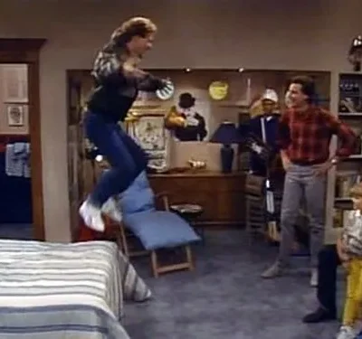 Um homem salta sobre a cama em uma sala de estar retrô. Várias pessoas, adultos e crianças, observam a cena animada.