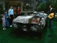 Família olha um carro conversível totalmente destruído e coberto de detritos em um gramado. Atmosfera de choque e surpresa.