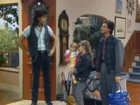 Um homem de colete e outro de jaqueta com duas meninas em casa. Ambiente familiar e descontraído.