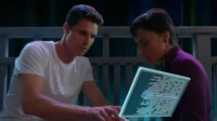 Homem e mulher concentrados em tablet holográfico com código, em cenário escuro e futurista.