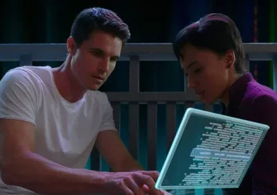 Homem e mulher concentrados em tablet holográfico com código, em cenário escuro e futurista.