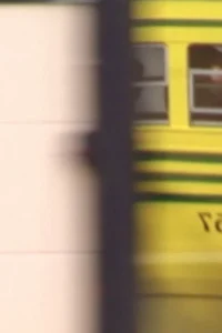 Um veículo amarelo borrado passa rapidamente por uma sombra escura, com um fundo claro à esquerda. Clima dinâmico.