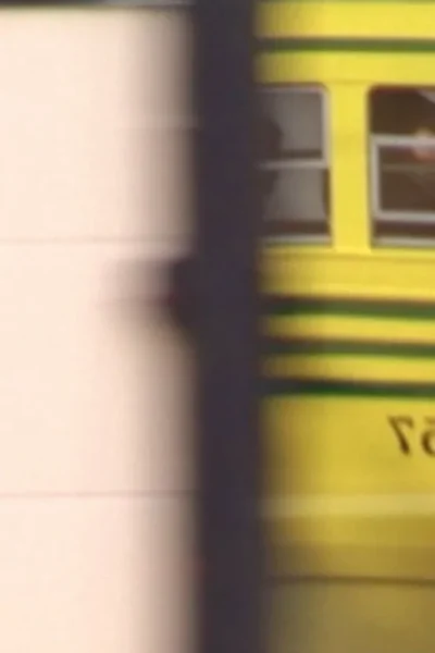 Um veículo amarelo borrado passa rapidamente por uma sombra escura, com um fundo claro à esquerda. Clima dinâmico.