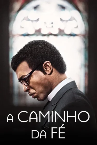 Homem negro de terno e óculos, com a cabeça baixa, em frente a uma janela de igreja iluminada. Clima sério e reflexivo.