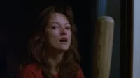 Mulher com cabelo bagunçado e olhar assustado, marca no nariz. Um taco de beisebol ao lado. Cenário escuro e tenso.