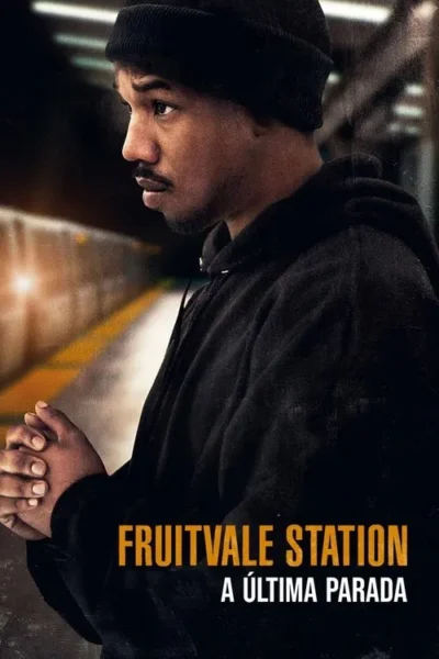 Jovem negro de gorro e moletom escuro, mãos entrelaçadas, olha à distância em plataforma de metrô sombria.