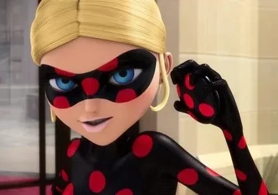 Heroína animada loira com traje preto de bolinhas vermelhas e máscara. Olhos azuis intensos, sorrindo confiante, punho cerrado.