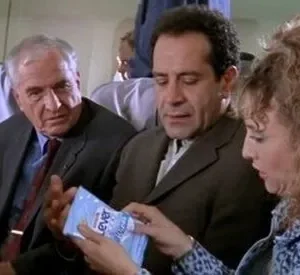 Em um avião, Monk examina um lenço umedecido, enquanto Sharona e Stottlemeyer o observam com curiosidade. Cena típica de Monk.
