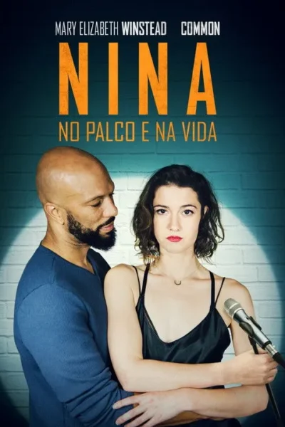Homem barbudo abraça mulher de microfone, que olha séria para frente. Fundo de parede de tijolos com foco de luz. Clima dramático musical.