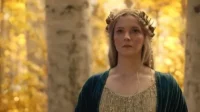 Galadriel de Os Anéis de Poder, loira com coroa de folhas douradas, olha séria em floresta outonal. Clima épico.
