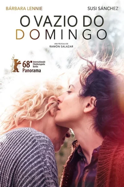 Duas mulheres, uma loira e uma morena, em abraço íntimo, com a morena se aproximando do rosto da loira. Fundo claro e suave.