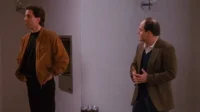 Jerry Seinfeld e George Costanza, de Seinfeld, em cenário simples. Jerry de jaqueta marrom; George gesticula com blazer.