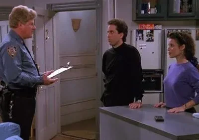 Em Seinfeld, um policial loiro com prancheta fala com Jerry e Elaine na cozinha. Eles parecem confusos.