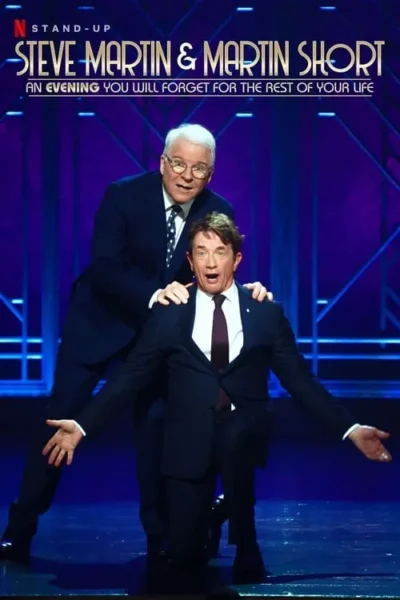 Dois homens de terno num palco azul. Um sorri por trás, com as mãos no outro, que está ajoelhado e com expressão exagerada e braços abertos.