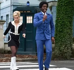 Doctor Who: Casal retrô dos anos 60, homem de azul e mulher de preto/branco, cruzam a Abbey Road. TARDIS azul ao fundo.