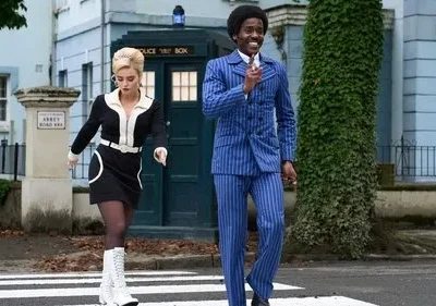 Doctor Who: Casal retrô dos anos 60, homem de azul e mulher de preto/branco, cruzam a Abbey Road. TARDIS azul ao fundo.