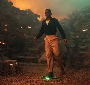 Homem elegante flutua em plataforma verde num cenário rochoso com fogo, exalando um clima de aventura sci-fi. Pôster de série/filme.