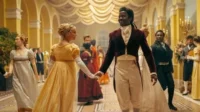 Doctor Who – T01E06:Ladino 5 Bridgerton:Um homem negro e uma mulher branca sorriem enquanto dançam de mãos dadas num salão de baile regencial dourado,com outros convidados.