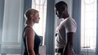 Cena de [Nome da Série/Filme]:mulher loira e homem negro trocam olhares tensos em um elegante cômodo com janelas grandes.