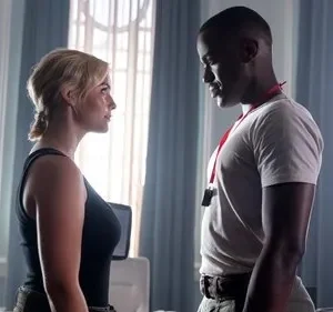 Cena de [Nome da Série/Filme]: mulher loira e homem negro trocam olhares tensos em um elegante cômodo com janelas grandes.