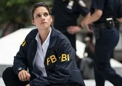 Agente do FBI Maggie Bell (Missy Peregrym) ajoelhada, observando atentamente num local de investigação, refletindo o tom sério da série FBI.