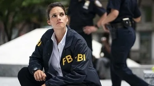 FBI – T01E04:Fogo Cruzado 1 Agente do FBI Maggie Bell (Missy Peregrym) ajoelhada,observando atentamente num local de investigação,refletindo o tom sério da série FBI.