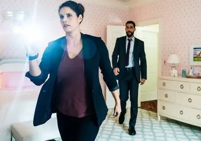 Em FBI, uma detetive com lanterna explora um quarto infantil rosa. Um agente de terno entra. Ambiente tenso de investigação.