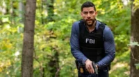Agente do FBI,com colete tático e arma,alerta em uma floresta. Pôster da série FBI com clima de investigação e ação intensa.