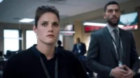 Mulher séria em primeiro plano e homem ao fundo em escritório tenso,com monitores. Imagem capta a urgência de uma série/filme de suspense.
