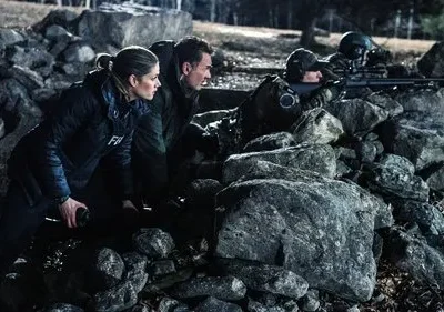 Agentes e atiradores em [Nome do Filme/Série] se abrigam atrás de uma parede de pedras, prontos para ação. Cena noturna tensa.