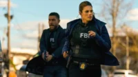 Agentes do FBI correm em uma rua urbana. A mulher no colete FBI e o homem com arma indicam uma cena de ação da série FBI.