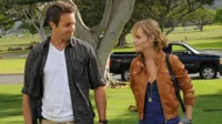 Em Hawaii Five-0,Alex O'Loughlin e Taryn Manning em um cemitério ensolarado. Ele sorri para ela,que tem olhar sério.
