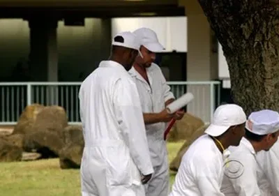 Aqui está uma opção concisa: Homens de macacão branco em Lost, alguns sentados, um em pé segurando um rolo de pintura, em um acampamento. Clima de trabalho ou cativeiro.