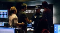 Havaí Cinco-0 – T01E15:Kai E'E (Maré) 10 Hawaii Five-0:Homens numa sala de controle. Um oficial da Guarda Costeira aperta a mão de um agente,com TSUNAMI WARNING na tela. Tensão e urgência.