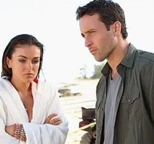 Em Hawaii Five-0, um homem e uma mulher de roupão, ambos com expressão séria, num cenário de praia ensolarada. Clima tenso.