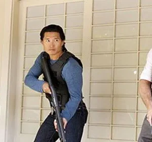 O time de Hawaii Five-0, Kono, Chin e Danno, alertas com coletes e armas, prontos para a ação.