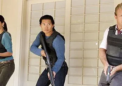 O time de Hawaii Five-0, Kono, Chin e Danno, alertas com coletes e armas, prontos para a ação.